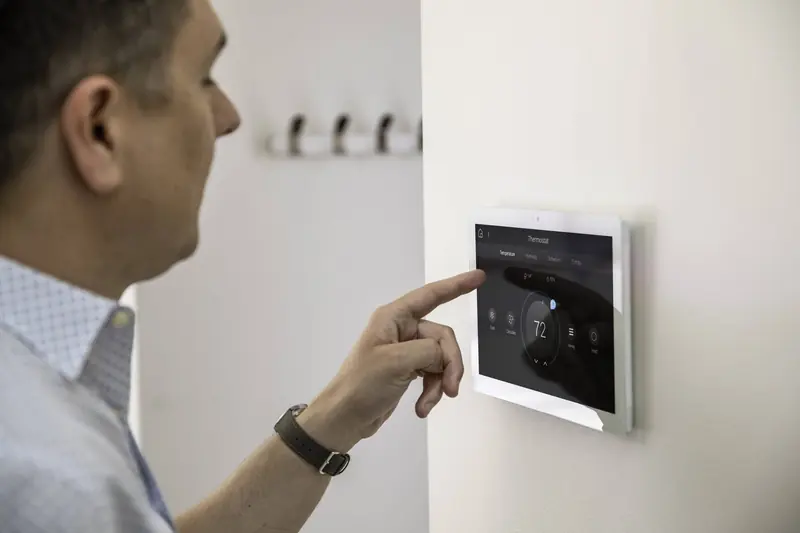 A man adjusting a wall-mounted smart thermostat touch screen